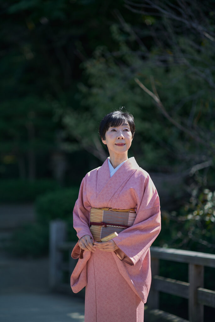 作家・武士道研究家・石川真理子。日本の伝統的な家屋の軒下で、柔らかな日差しを受けながら遠くを見つめる美しい着物姿。