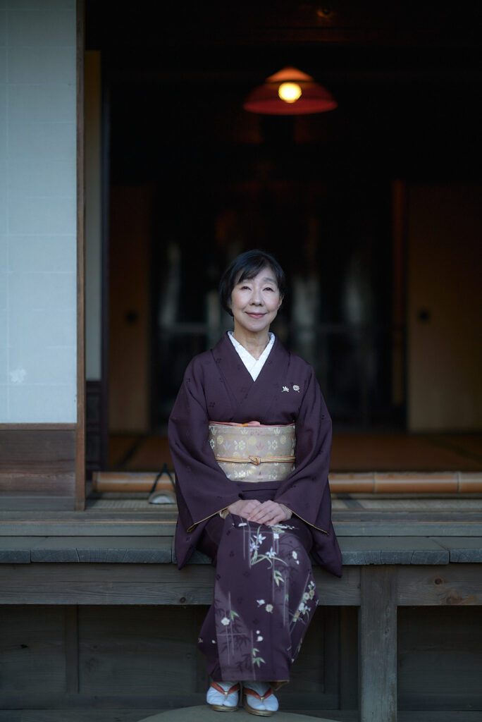 「経年美化」を体現する、着物姿の石川真理子のポートレート。古い日本家屋の縁側で穏やかに微笑む姿が、武家の教えである「婦容（ふよう）」と内面からの美しさを象徴している。（撮影：写真家 魚住心 / Leica）