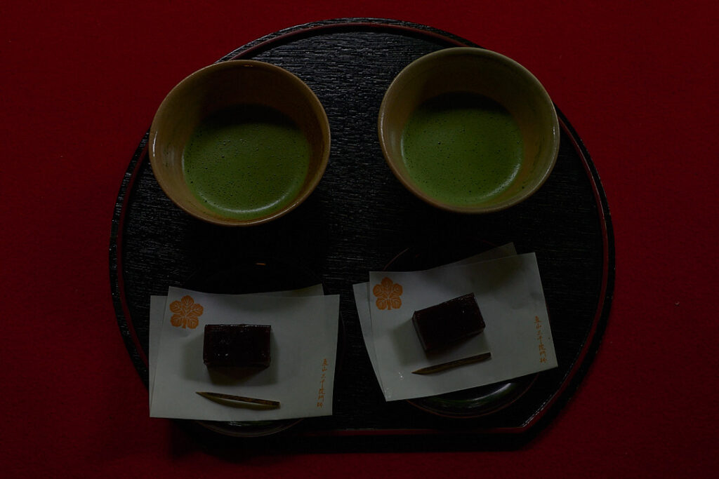 赤毛氈の上に静かに並べられた二つの抹茶茶碗と和菓子。適切な「間（ま）」を保ちながら存在する様子が、熟年夫婦の理想的な距離感と、武士道における「人間（じんかん）」の関係性を象徴している。撮影：写真家 魚住心（Leica）