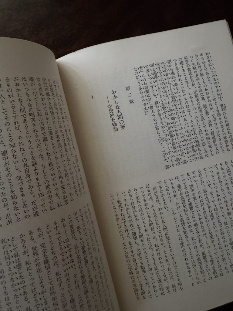 書物の縦書きのページを開き、「第二章 おかしな人間の夢 ――空想的な物語」という見出しが印刷されている様子を斜めから撮影した写真。