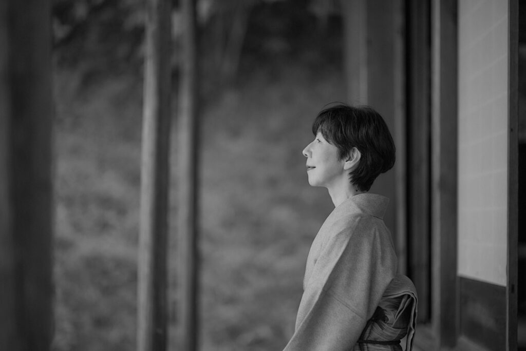 背景の深い森を見つめる、着物姿の石川真理子の穏やかな横顔（モノクロ写真）