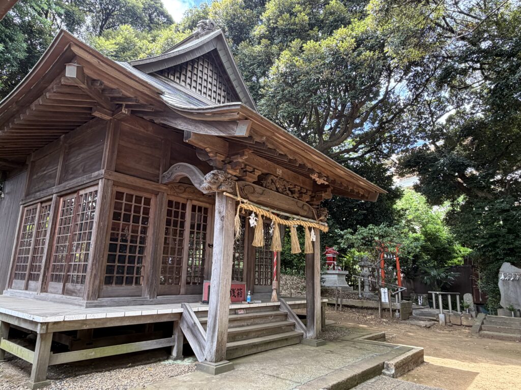 豊かな木々に囲まれた鹿島神社の木造の拝殿。しめ縄が飾られ、静謐な空気が漂っている。

